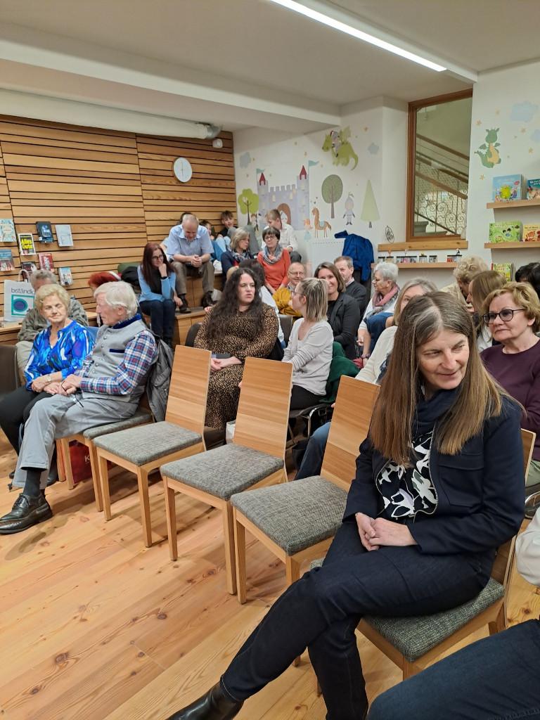 Foto vom Publikum auf Stühlen sitzend. 3 Stühle vorne noch leer